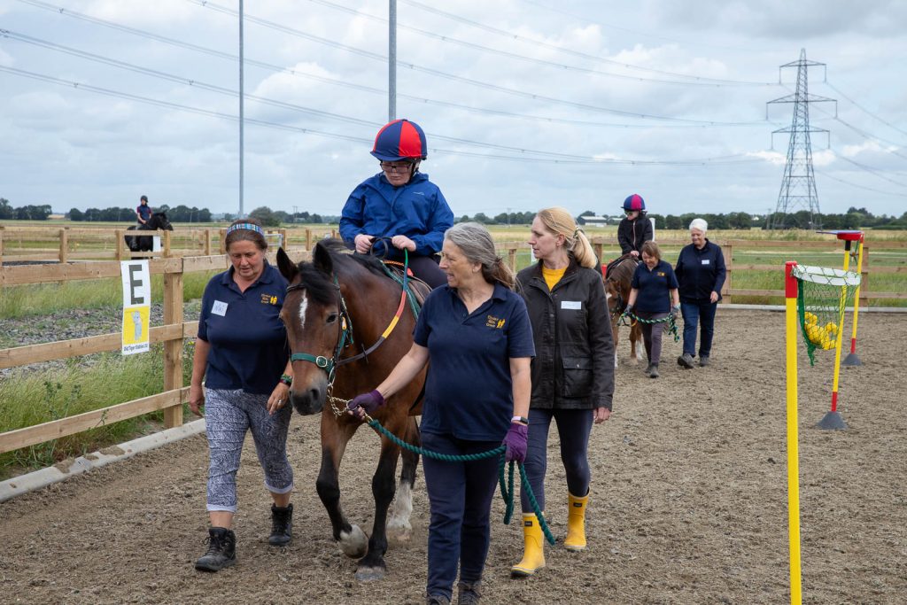 Image of young rider on horse back with the team of three volunteers that provide any assistance the rider needs