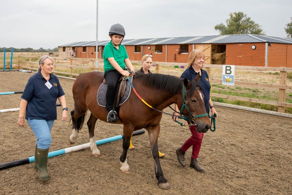 Young rider on a pony walking over poles, supported by volunteer helpers